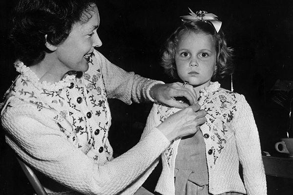 Actress Maureen O'Sullivan buttons up her daughter Mia Farrow's matching cardigan.  (Photo by Keystone/Getty Images)
