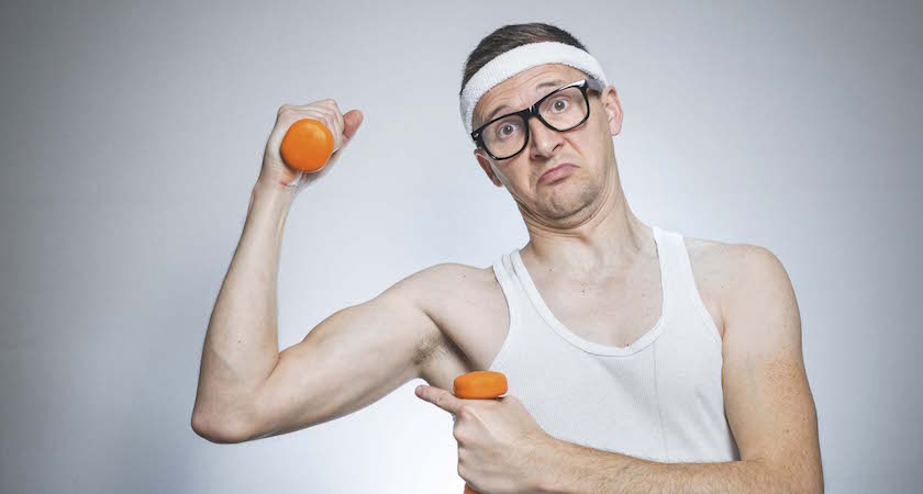 Nerd man showing his small biceps over gray background. Funny sport weak male ready for exercising - training