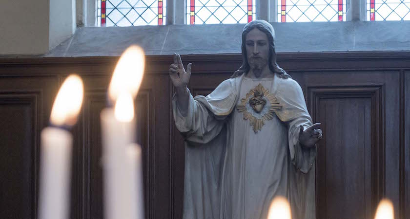 Statue of Jesus Christ in Church with Lit Burning Candles in Foreground