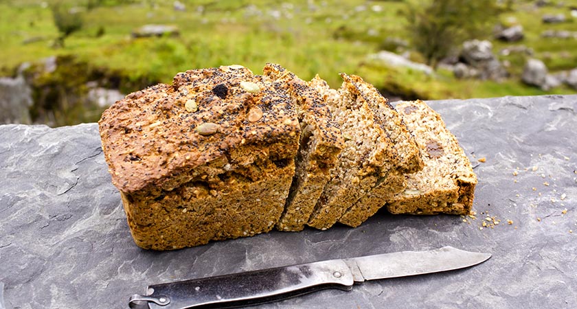 Sliced loaf of the fresh traditional Irish soda bread outside with knife aside and visible greenery on the background.