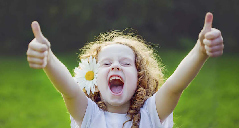 Laughing girl with daisy in her hairs, showing thumbs up.