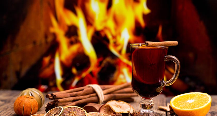 Glass of christmas mulled wine on wooden table against fireplace