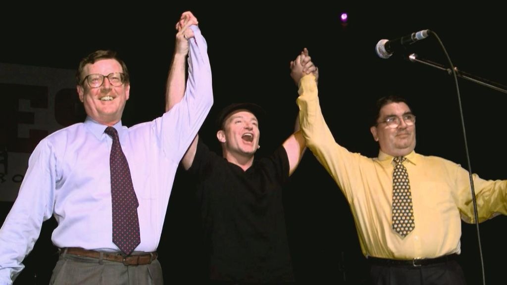 Bono (C) holds up the arms of Ulster Unionist leader David Trimble (L) and SDLP leader John Hume on stage during a concert 