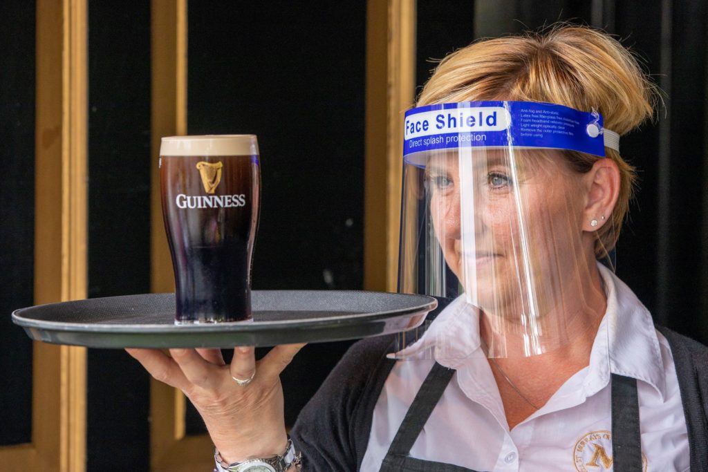 PPE on staff member holding pint of Guinness in Irish pub