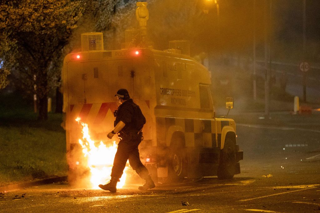 A police officer walks behind a police vehicle with flames leaping up the rear after violence broke out in Newtownabbey, north of Belfast, in Northern Ireland on April 3, 2021. - The disturbance in the Loyalist area north of Belfast, where petrol bombs were thrown and cars were set alight, follows a night of violence in the Northern Ireland capital in which police officers were injured prompting calls for calm. It is thought rising discontent among unionist pro-British factions in Northern Ireland over arrangements aimed at preserving a fragile peace in the territory by preventing a hard border with EU member Ireland is fueling anger. Tension has also been stoked this week by a decision not to prosecute 24 Sinn Fein party members who attended the funeral in June of Irish Republican Army figure Bobby Storey in blatant violation of of Covid-19 guidelines.